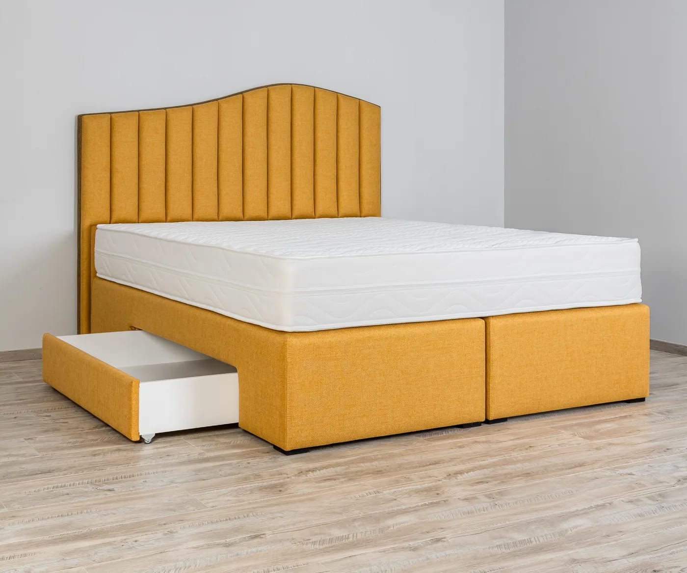 Krevet s punom boxspring bazom do poda; lijeva bočna ladica na kotačićima izvučena je i vidi se bijela unutrašnjost.